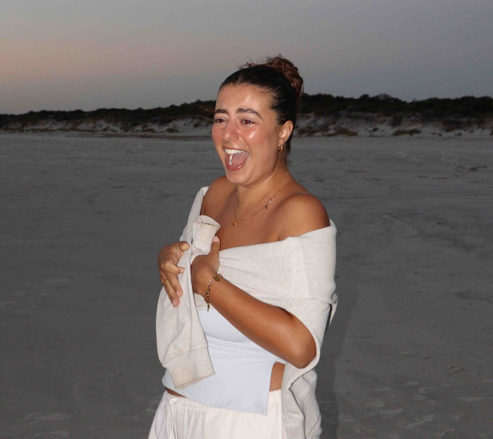 A portrait of a young female backpacker smiling on a beach with moonlight above
