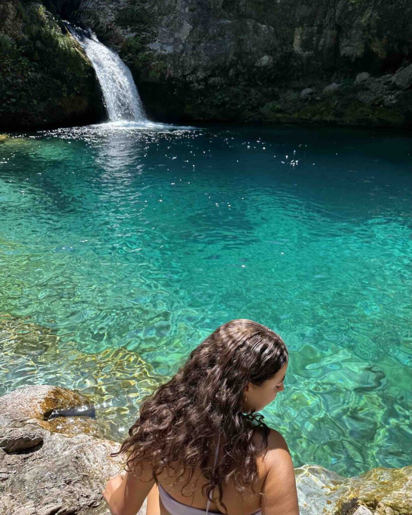 A girl sitting in front of the Blue Eye in Theth with crystal clear turquoise water in the Albanian Alps