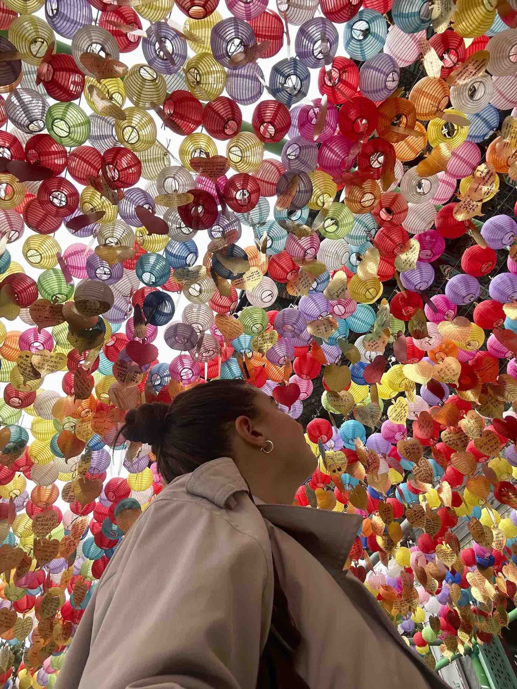 A female backpacker standing underneath a ceiling of colorful mini lanterns in Busan South Korea at the Haedong Yonggungsa Temple