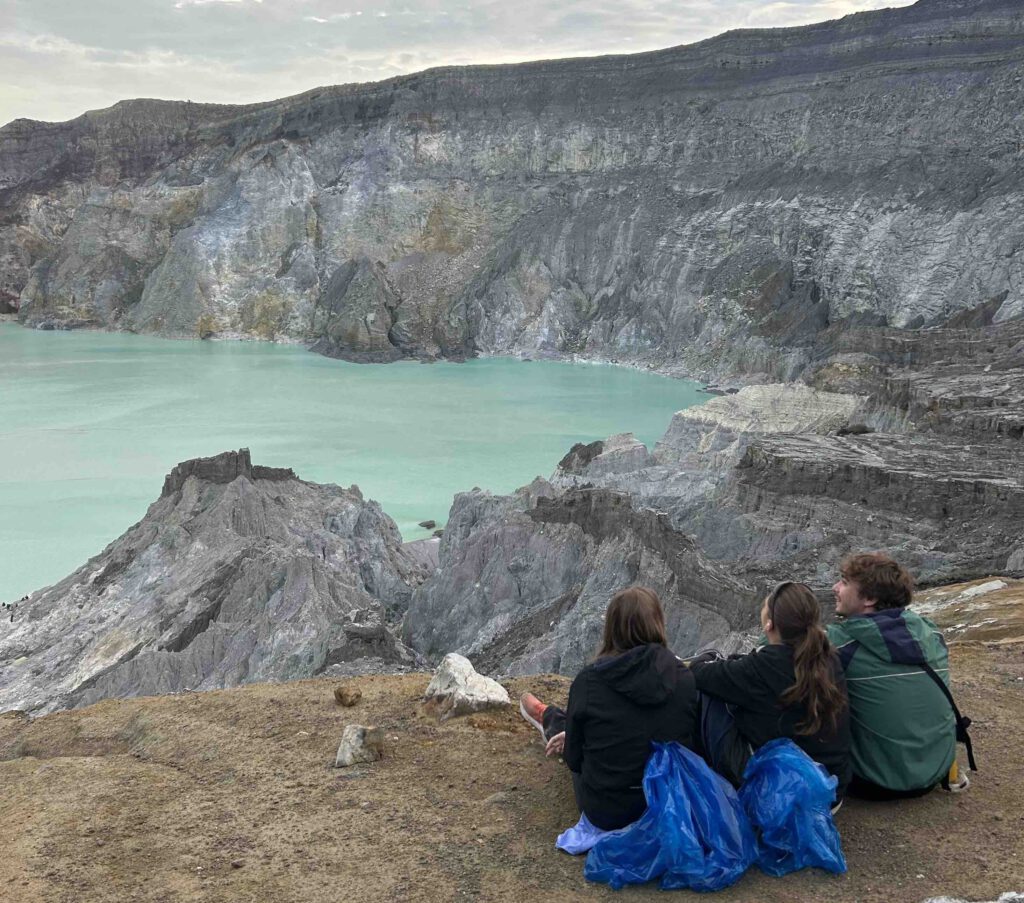 Group of travellers sitting by the turquoise crater lake at Mount Ijen East Java at sunrise