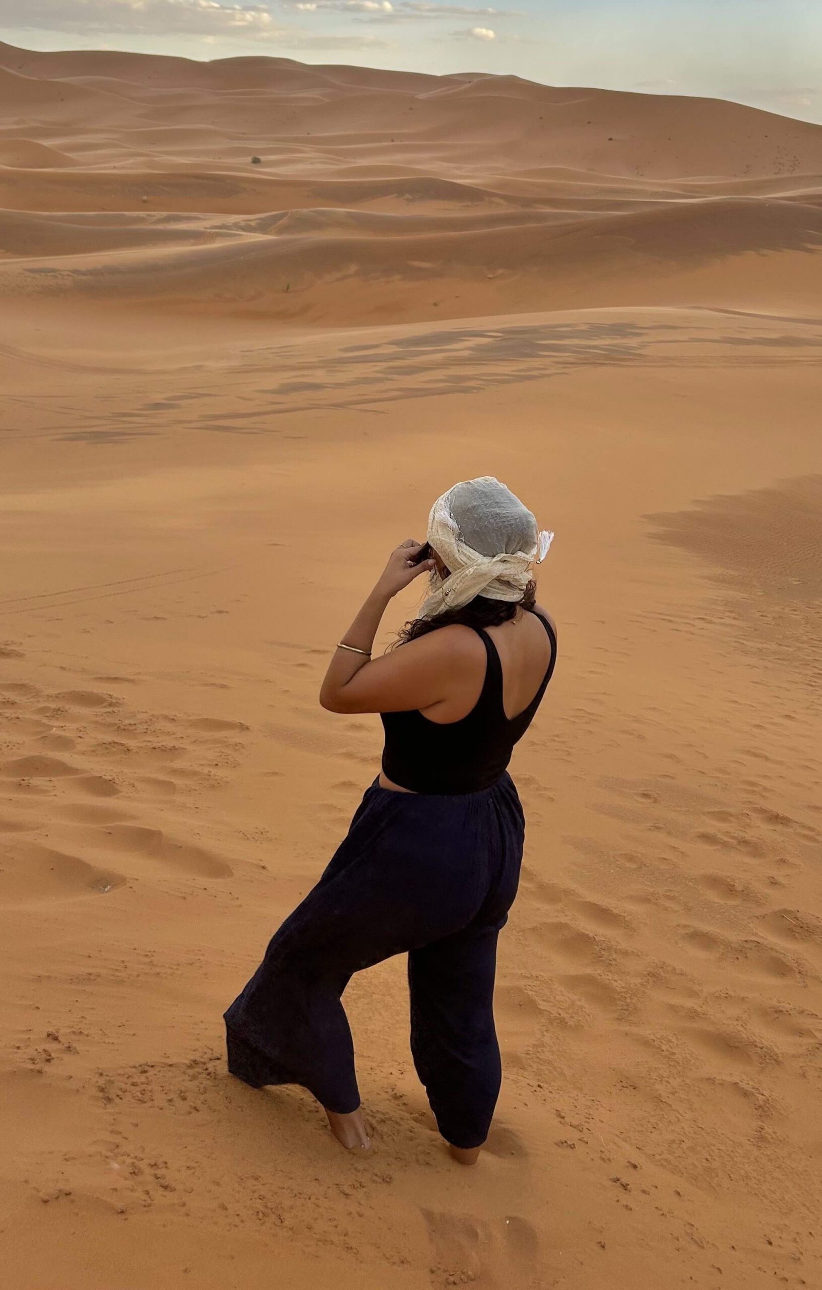 A young women standing on sand dunes in the Moroccan Sahara desert wearing a headscarf