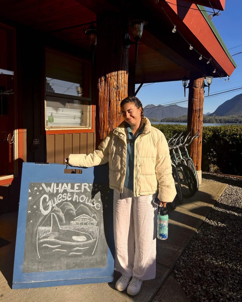 Solo female traveller posing with sign outside of Whalers Guesthouse Tofino Hostel British Columbia in spring