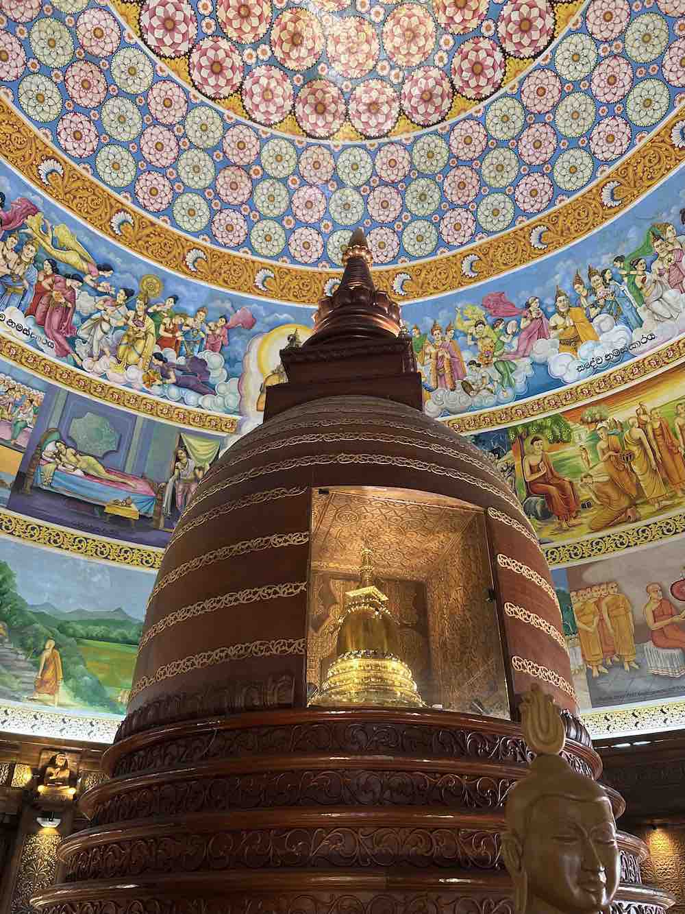 A Buddhist Stupa in a temple in Kandy Sri Lanka with colorful images on the ceiling above