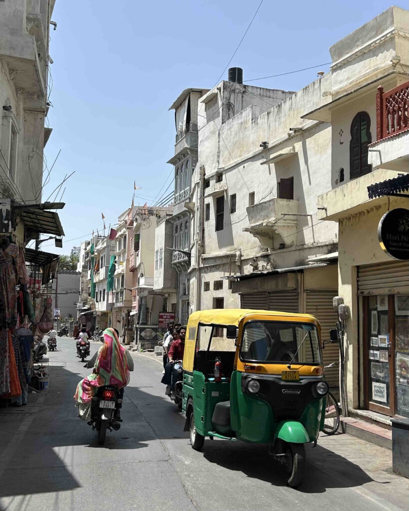 A tuk tuk driving and women on motorbike in the streets of Udaipur India